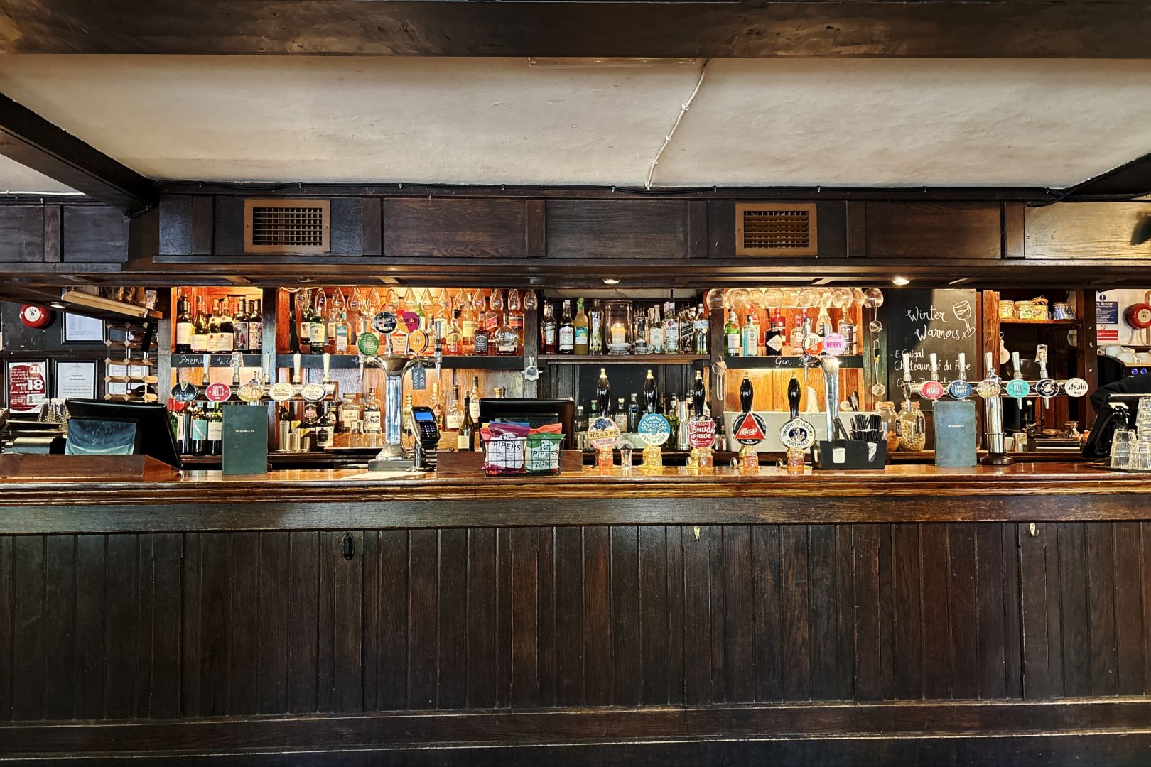 The bar at the Spaniard’s Inn, Hampstead Heath: dark wood and beer taps, with rows of bottles of spirits and wine on the shelves behind.